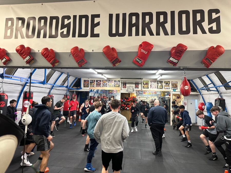 Members training at Broadside Warriors gym beneath a large 'Broadside Warriors' sign with a row of red boxing gloves